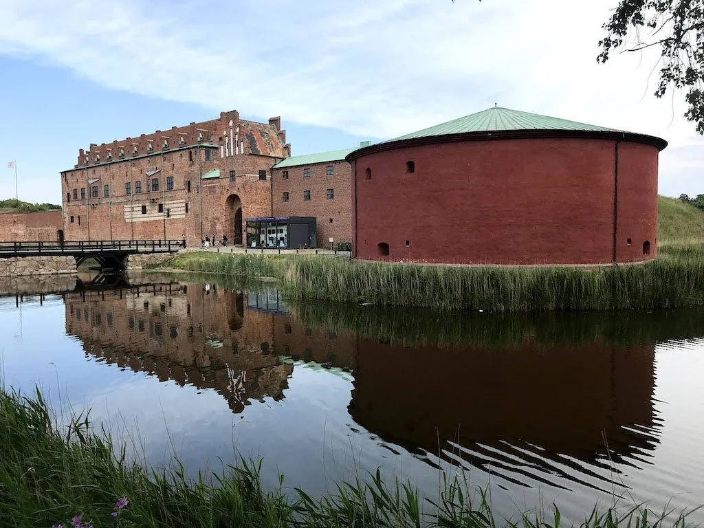 Large imposing fortress with red walls, with its reflection visible in the water around it.